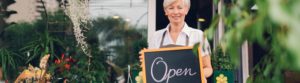 GettyImages 477952776 1 300x83 - Smiling mature woman holding open sign at flower shop