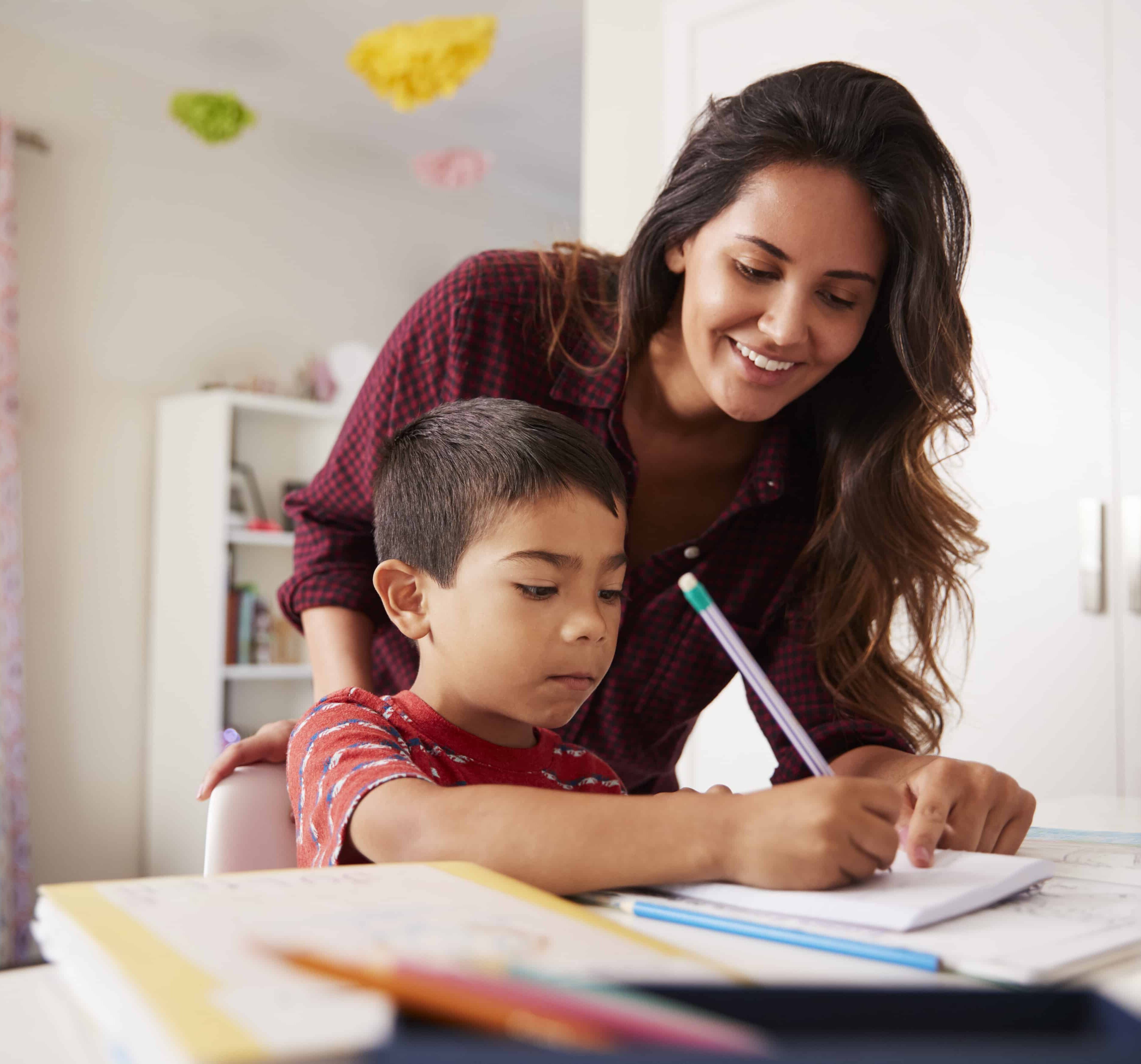 Mother Helping Son With Homework Sitting At Desk In Bedroom