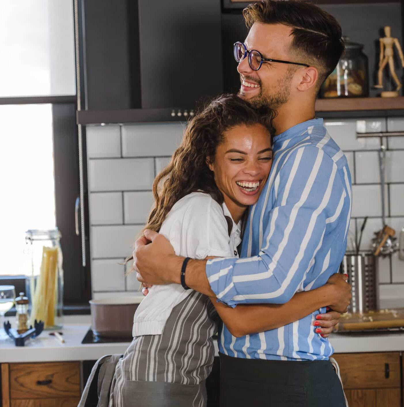 Young cheerful multi-ethnic couple preparing pasta together at their modern kitchen